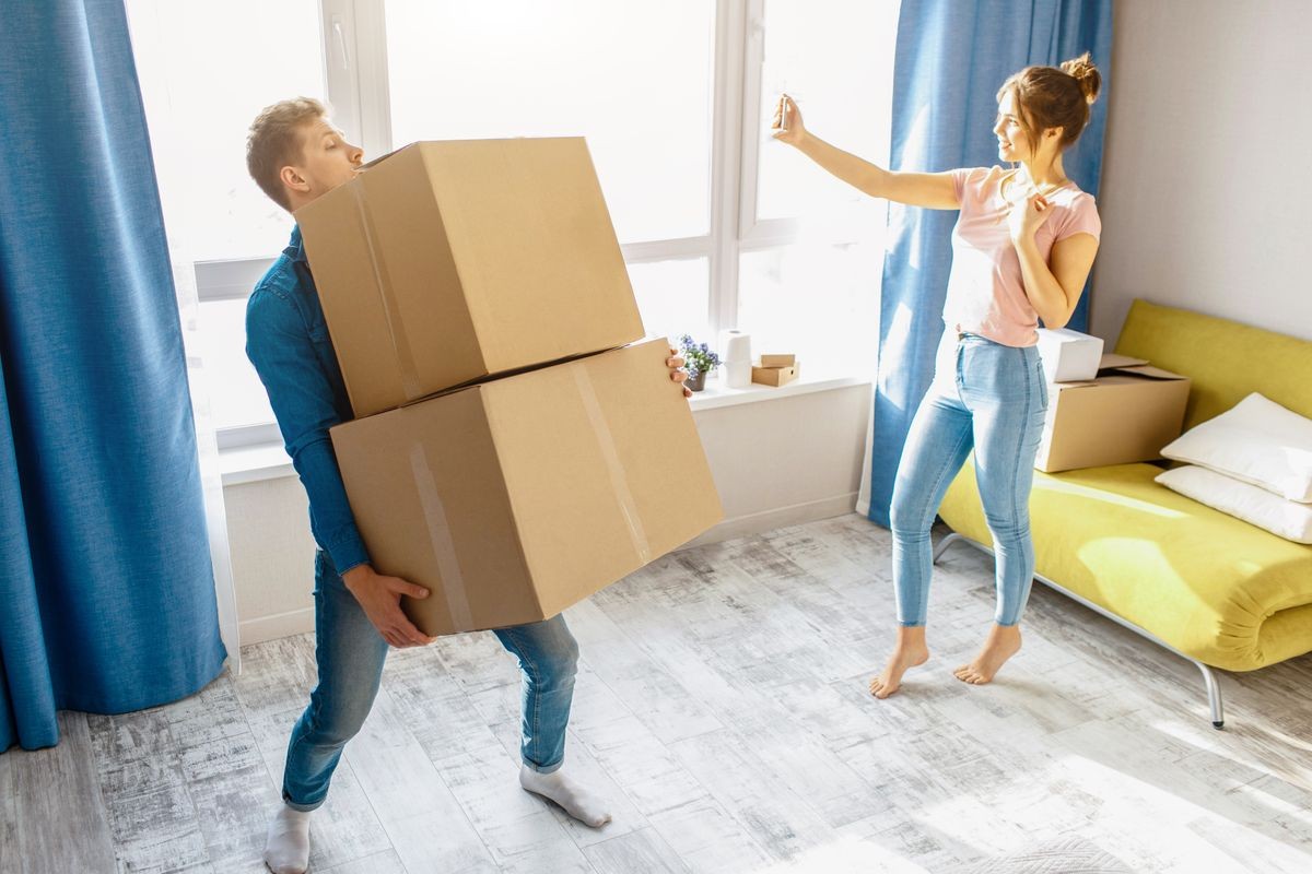 Young family couple bought or rented their first small apartment. Guy carry heavy boxes alone. Young woman take selfie at window and have fun. Unfair work. Moving and unpacking.